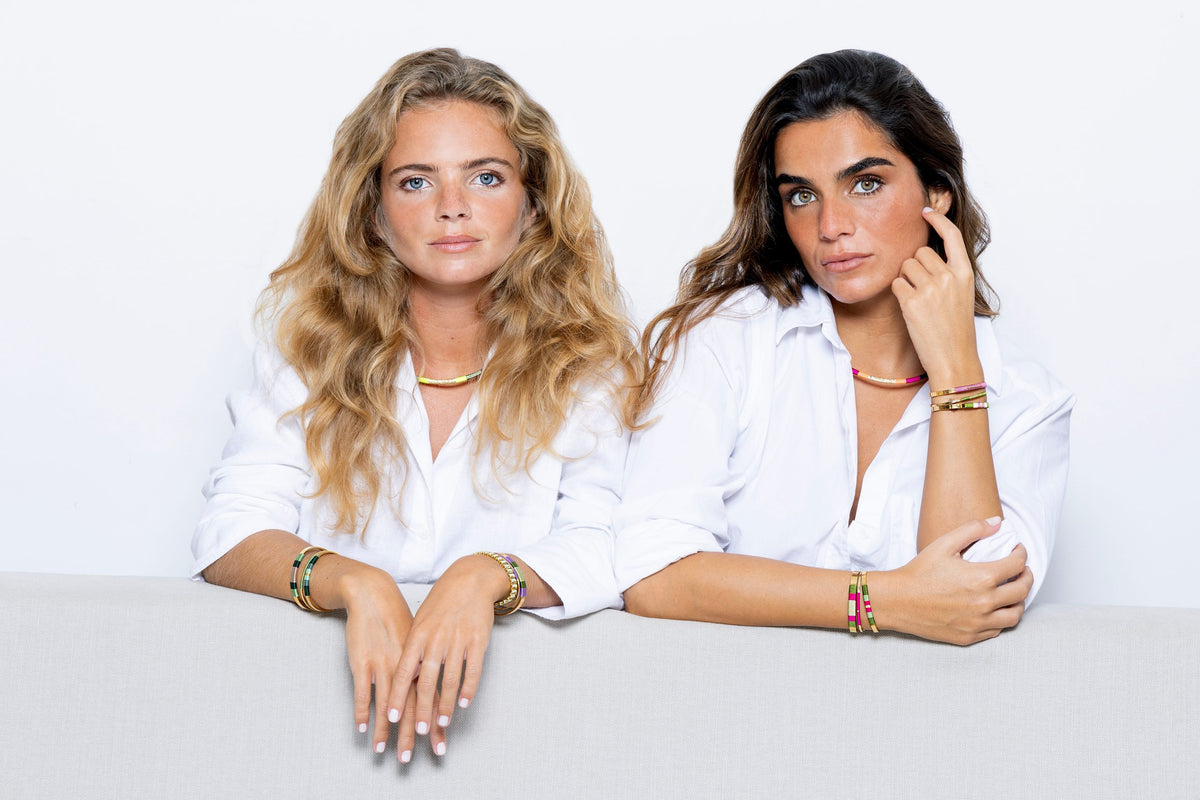 Duas mulheres de camisa branca com pulseiras Kapim coloridas nos pulsos